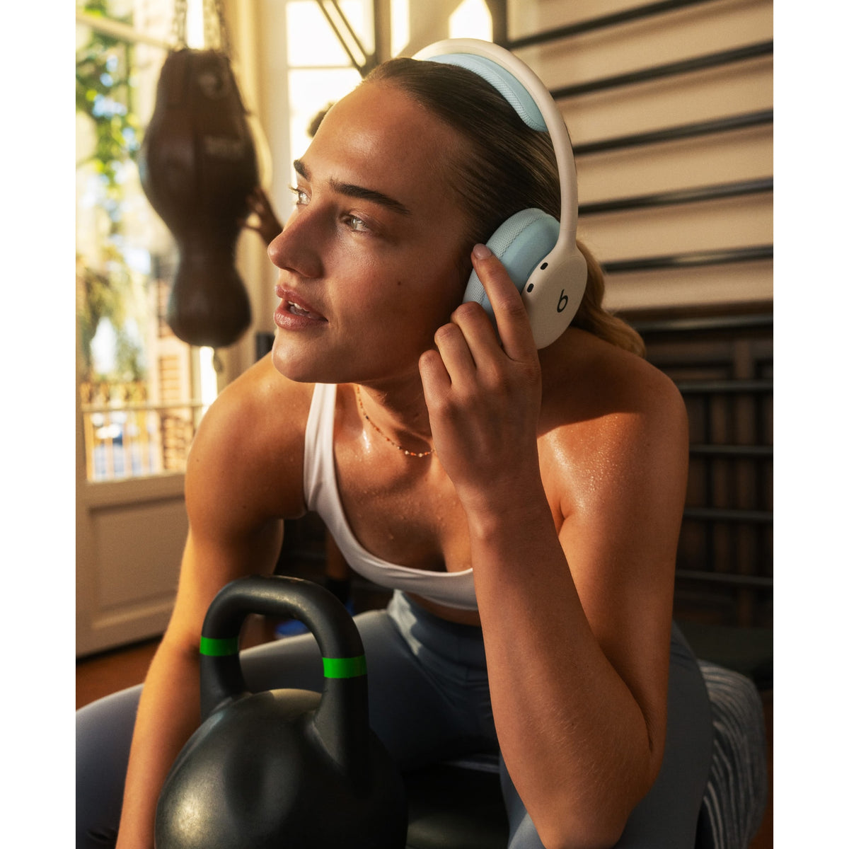 Woman wearing light blue Beats 360 headphones while lifting weights in gym